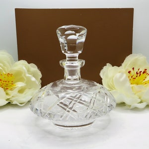 May include: A clear glass bottle with a cut glass design. The bottle has a round base and a tall, cylindrical neck with a stopper.