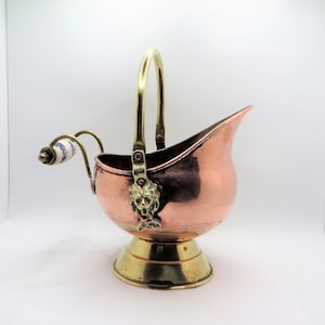 May include: A copper and brass coal scuttle with a lion head design on the handle. The scuttle has a white and blue porcelain handle.