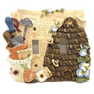 May include: A decorative light switch cover with a garden theme. The cover features a brown wicker basket with blue flowers, a pot with gardening tools, and a seed packet. The switch cover is made of resin and has a textured finish.