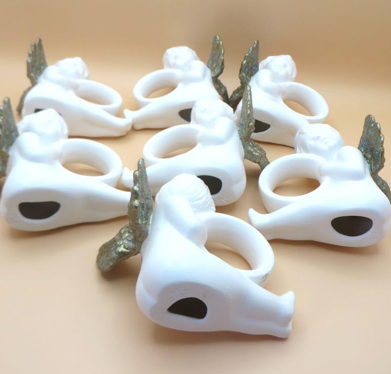 Pu&ograve; includere: Una collezione di sette portatovaglioli a forma di angelo in ceramica bianca. Ogni anello presenta un angelo reclinato con ali color oro. I portatovaglioli hanno un'apertura circolare per un tovagliolo e un'apertura ovale scura sul fondo.