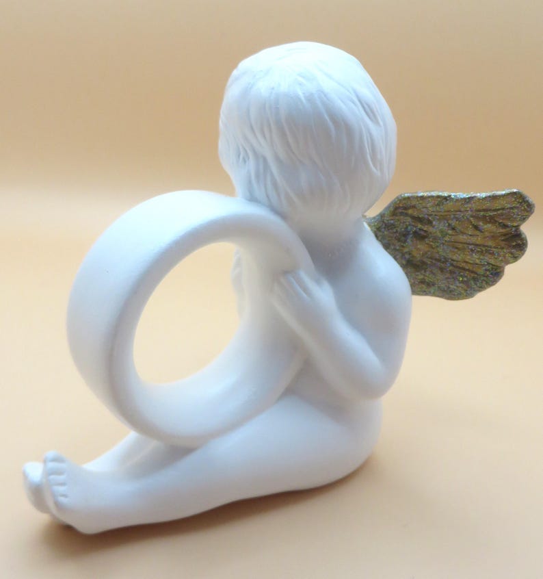 Pu&ograve; includere: Una statuetta di cherubino bianco che tiene un anello bianco. Il cherubino ha ali color oro ed &egrave; seduto con la schiena rivolta allo spettatore. La statuetta &egrave; realizzata in un materiale liscio e opaco.