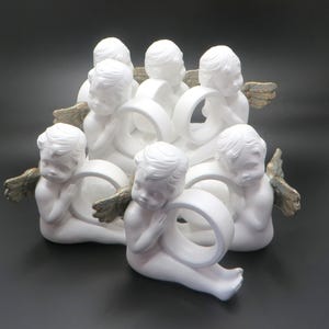 Pu&ograve; includere: Un centrotavola in ceramica bianca con otto figure di cherubini. Ogni cherubino tiene un anello bianco, con ali color oro. I cherubini sono disposti in un motivo circolare, creando un design decorativo ed elegante.