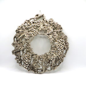 Peut inclure: Couronne en métal argenté avec un motif de vigne. La couronne est faite d'un travail de métal complexe et présente des grappes de raisins et des feuilles.