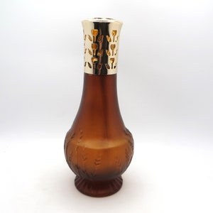 Peut inclure: Une bouteille de diffuseur d'huile en verre brun avec un dessus en métal doré et un motif floral. La bouteille a une base large et un col étroit.