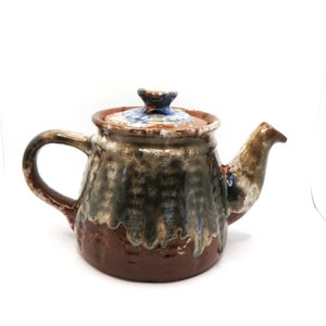 May include: A brown ceramic teapot with a blue and white glaze. The teapot has a rounded body and a spout on the side. The lid is also ceramic and has a blue knob.