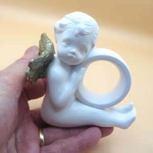 Pu&ograve; includere: Statuina di angelo in ceramica bianca con ali color oro. L'angelo &egrave; in posizione seduta, con un design a forma di anello incorporato. La statuina &egrave; tenuta in mano.