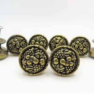 Peut inclure: Ensemble de six boutons de cabinet en laiton antique avec un motif en relief de fruits et de raisins. Les boutons sont ronds et ont une finition lisse et polie.