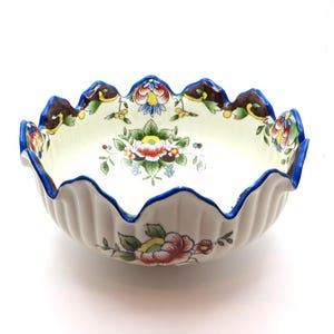 May include: A white ceramic bowl with a scalloped rim, adorned with a blue border and floral patterns. The bowl features a fluted exterior and a central floral design, showcasing a vintage aesthetic.
