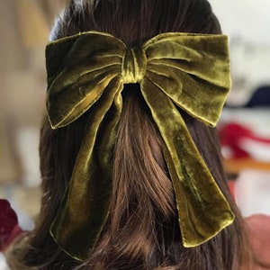 May include: A large, olive green velvet bow hair clip. The bow is tied in a classic style with long tails.