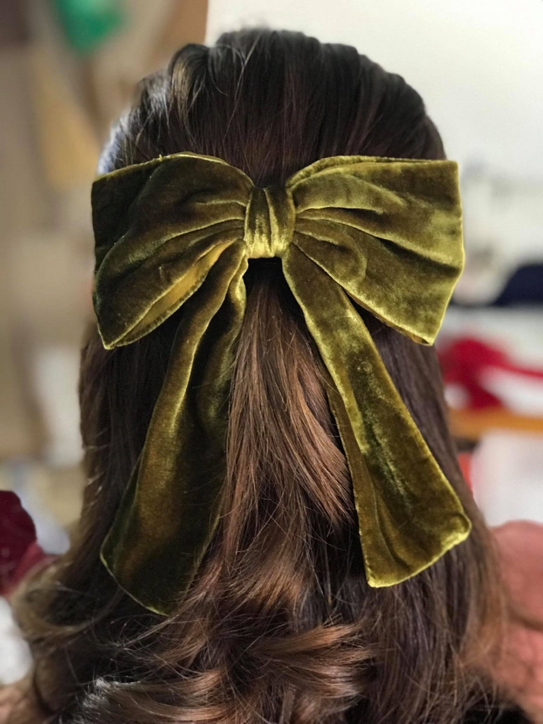 May include: A large, olive green velvet bow hair clip. The bow is tied in a classic style with long tails.
