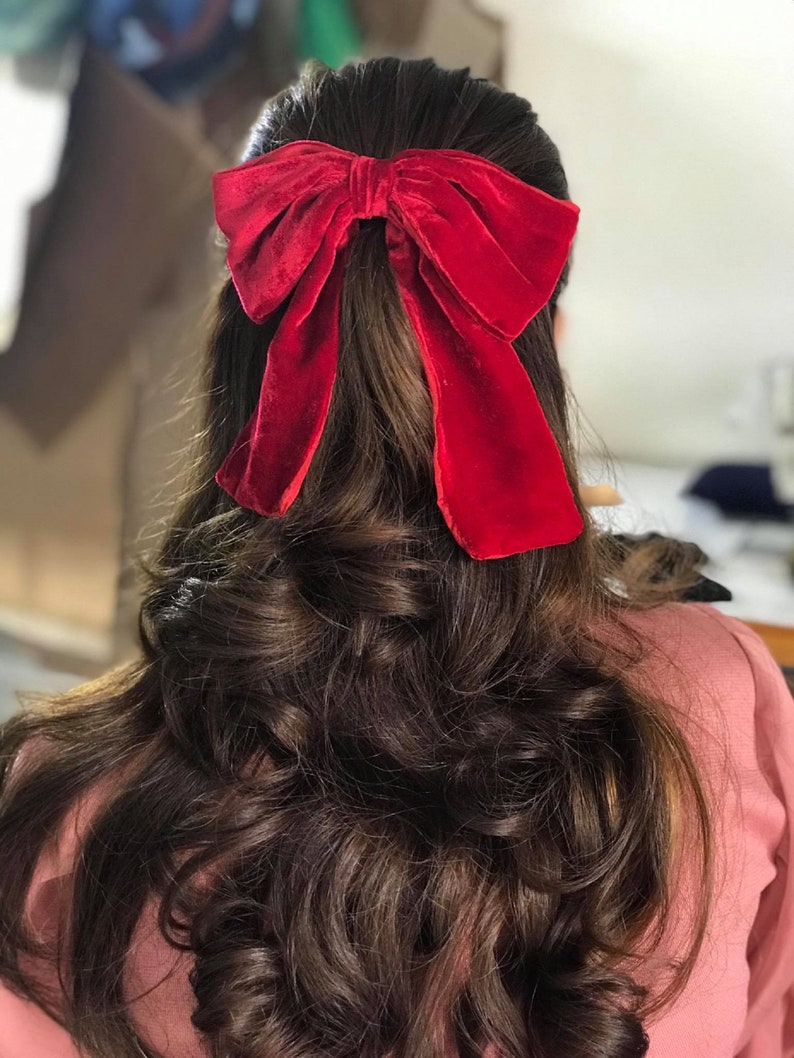 May include: A woman with long, dark brown hair wearing a red velvet bow in her hair.