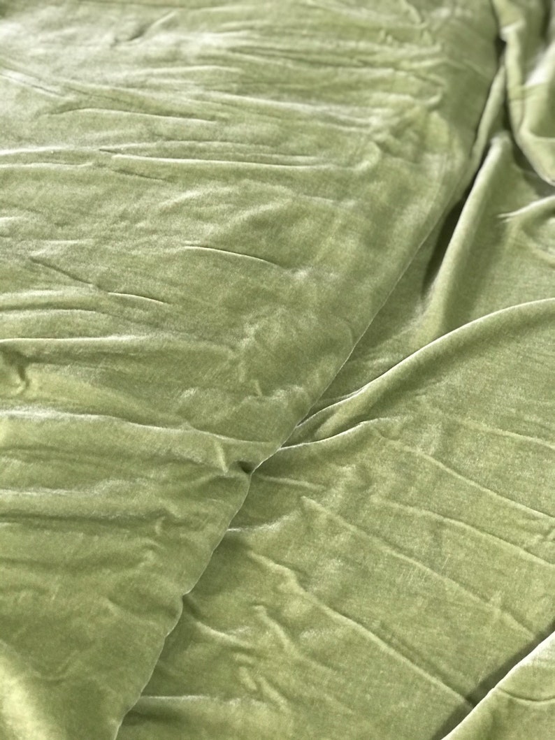 Puede incluir: Primer plano de una tela de terciopelo verde suave con una textura lisa. La tela est&aacute; doblada y drapeada, creando un aspecto lujoso y elegante.