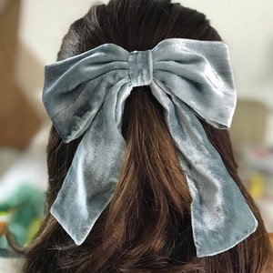 May include: A large, light blue velvet bow hair clip. The bow is tied in a large, loose knot and has long, flowing tails.