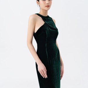 May include: A dark green velvet gown with a high neckline and a unique shoulder cutout. The dress is form-fitting and floor-length, showcasing a sleek and elegant silhouette. The fabric has a rich, luxurious sheen, perfect for formal events.