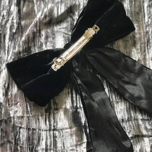 May include: A black velvet hair bow with a silver clip. The bow has a long tail that is tied in a knot.