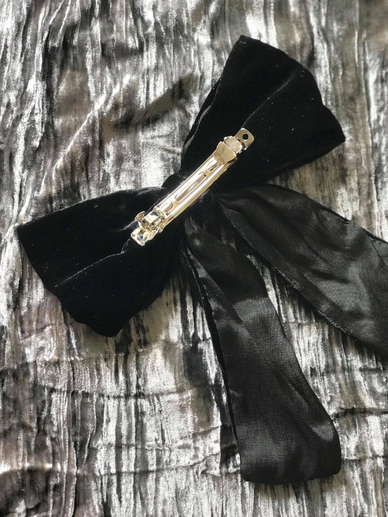 May include: A black velvet hair bow with a silver clip. The bow has a long tail that is tied in a knot.