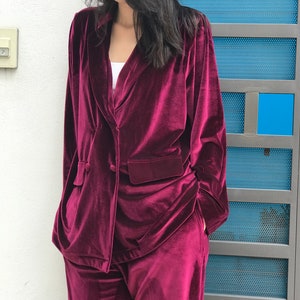 May include: A burgundy velvet blazer and matching pants. The blazer has a double-breasted closure and a pocket on the left side. The pants have a wide leg.