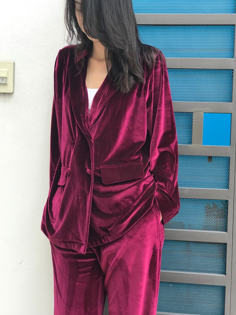 May include: A burgundy velvet blazer and matching pants. The blazer has a double-breasted closure and a pocket on the left side. The pants have a wide leg.