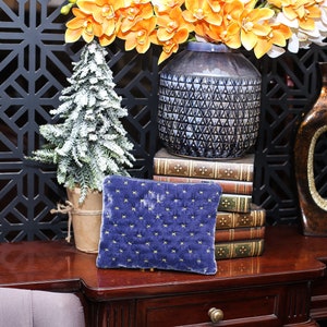 May include: A blue velvet cushion with gold stars on a wooden table with a stack of books, a vase of orange flowers, and a decorative vase.