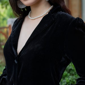 Pode incluir: Uma mulher vestindo um blazer de veludo preto com um colar de p&eacute;rolas e um par de brincos pendurados.