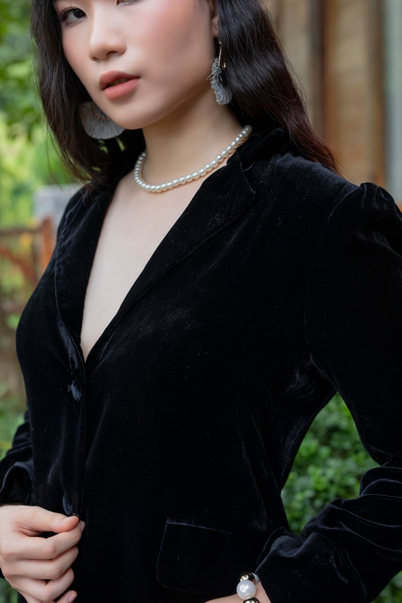 Pode incluir: Uma mulher vestindo um blazer de veludo preto com um colar de p&eacute;rolas e um par de brincos pendurados.
