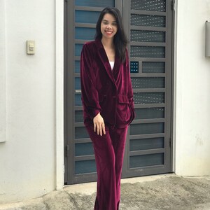 May include: A woman wearing a burgundy velvet blazer and matching pants. The blazer has a double-breasted closure and the pants have a wide leg.