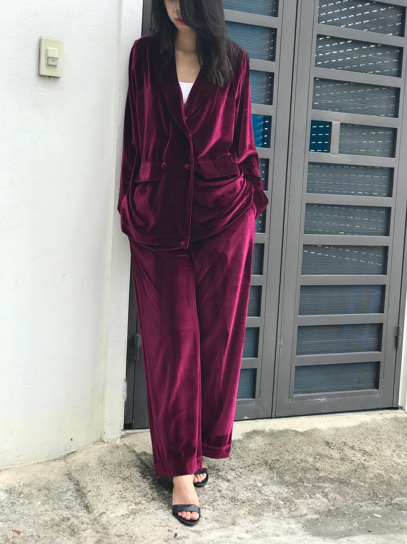 May include: A burgundy velvet blazer and matching pants. The blazer has a double-breasted closure and a notched collar. The pants have a wide leg.