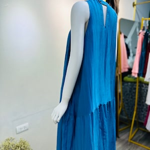 May include: A sleeveless maxi dress in a vibrant blue color. The dress has a simple design with a V-shaped back opening and a tiered skirt.