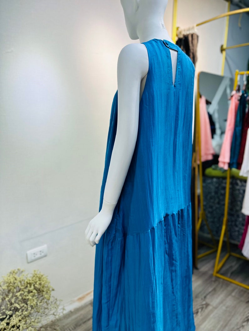 May include: A sleeveless maxi dress in a vibrant blue color. The dress has a simple design with a V-shaped back opening and a tiered skirt.