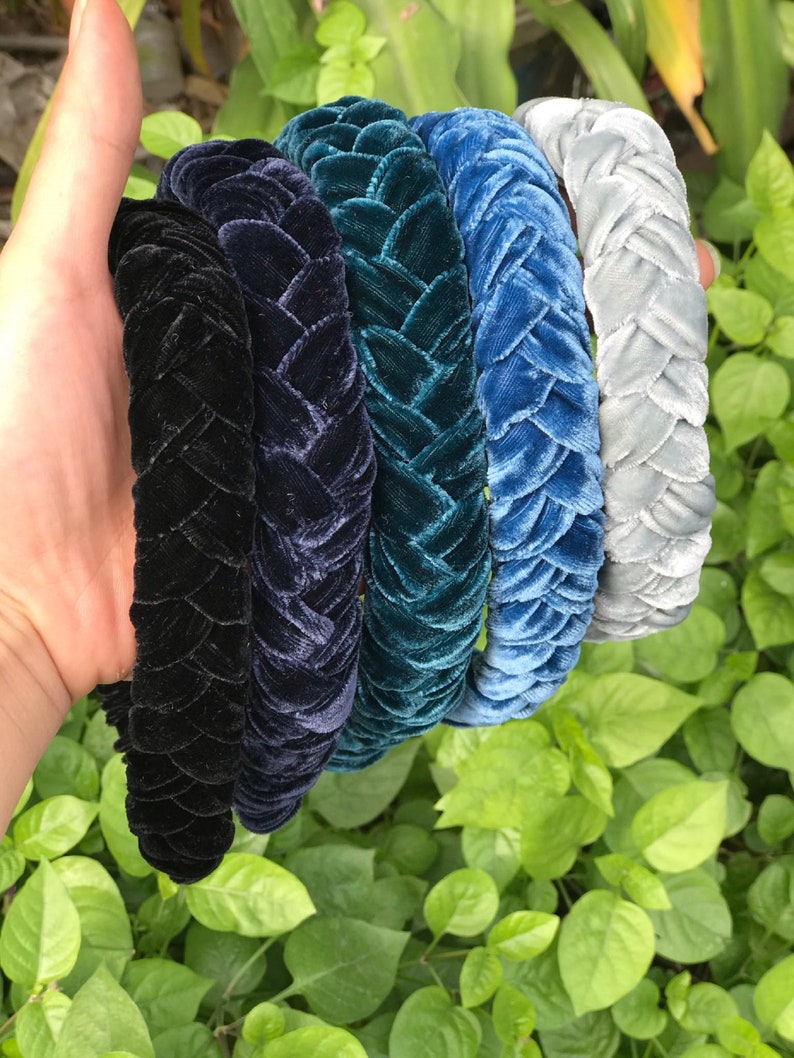 May include: Five braided velvet headbands in various shades of blue, teal, and black. The headbands are arranged in a stack, with the lightest color on top and the darkest color on the bottom.