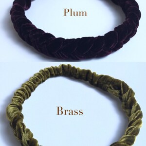 May include: Two velvet headbands, one in a dark plum color and the other in a dark olive green color. The headbands are braided and have a stretchy fit.