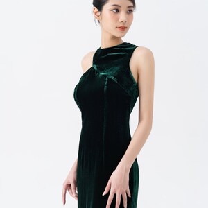 May include: A dark green velvet gown with a high neckline and sleeveless design. The dress has a fitted bodice and a flowing skirt. The fabric has a soft, luxurious texture. The dress is suitable for formal events.
