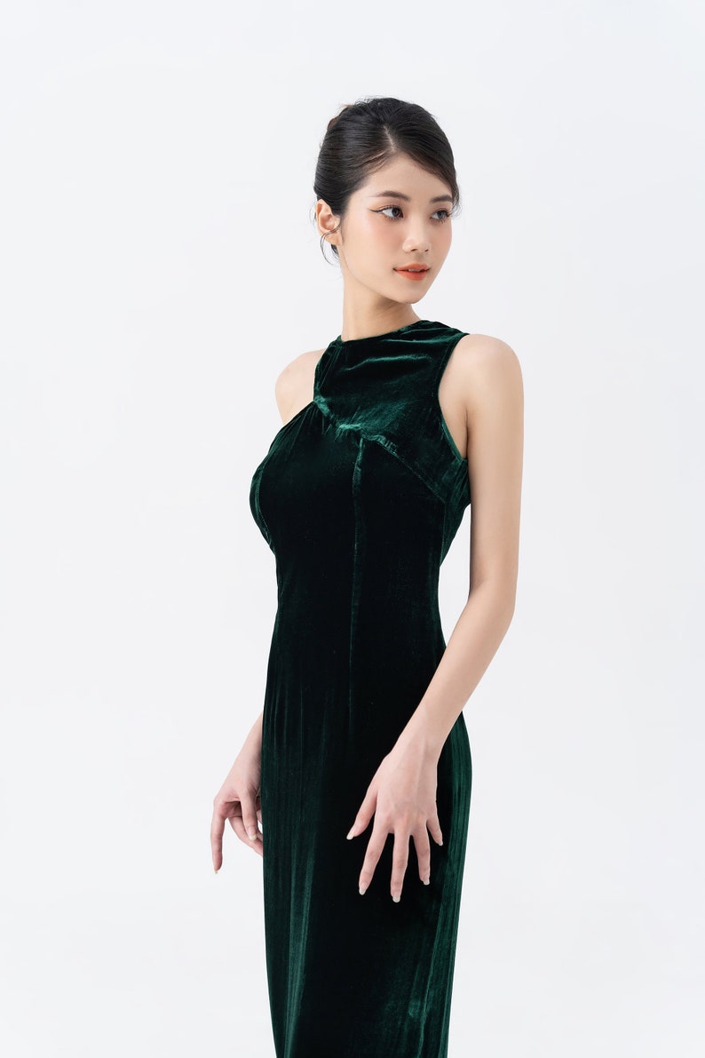 May include: A dark green velvet gown with a high neckline and sleeveless design. The dress has a fitted bodice and a flowing skirt. The fabric has a soft, luxurious texture. The dress is suitable for formal events.