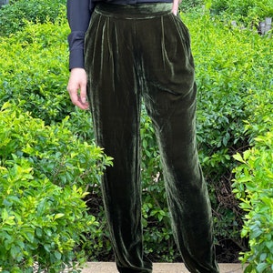 May include: A pair of dark green velvet pants with a high waist and a pleated front. The pants are fitted through the legs and have a slightly cropped length.