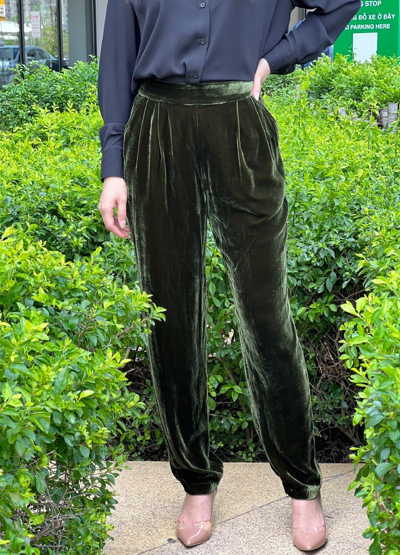 May include: A pair of dark green velvet pants with a high waist and a pleated front. The pants are fitted through the legs and have a slightly cropped length.
