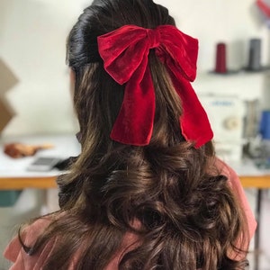 May include: A woman with long, brown, curly hair wearing a red velvet bow in her hair.