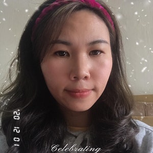 May include: A woman with long dark hair is wearing a pink velvet headband. She is smiling and looking at the camera. The text "Celebrating B612 DAY" is written on the image.