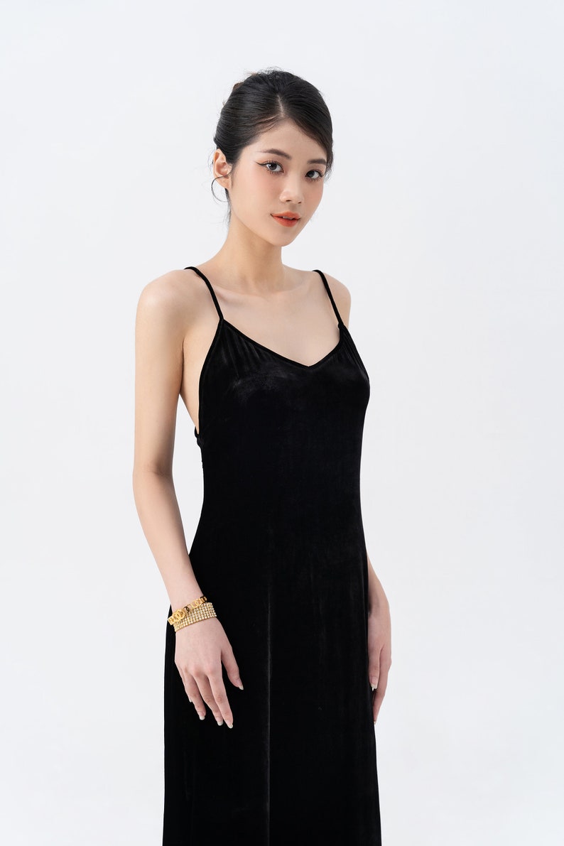 May include: A woman wearing a black velvet maxi dress with thin straps. She is wearing a gold bracelet on her left wrist.