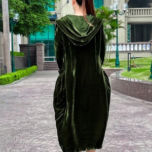 May include: A long, dark green velvet hooded dress with a loose, flowing silhouette. The dress has a gathered skirt and a relaxed fit.