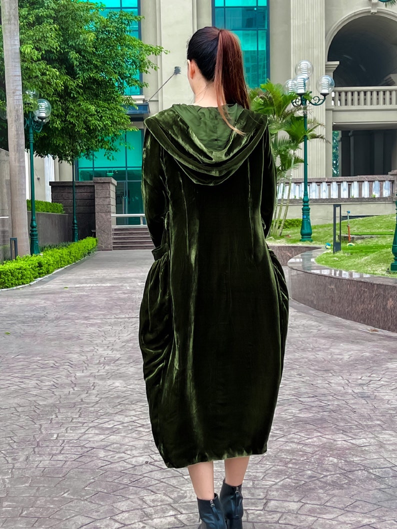 May include: A long, dark green velvet hooded dress with a loose, flowing silhouette. The dress has a gathered skirt and a relaxed fit.