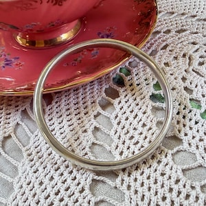 May include: A smooth, circular silver-toned bangle bracelet with a polished metallic finish. The bracelet is a simple, continuous band without any additional embellishments, clasps, or decorative patterns, presenting a clean and uniform appearance.