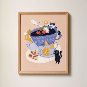 Può includere: Un'illustrazione incorniciata di una tazza da tè blu con un motivo floreale e limoni. Tre gatti giocano intorno alla tazza da tè, uno è arancione e due sono neri.