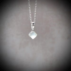 May include: A silver chain necklace featuring a small, square-shaped pendant with a smooth, translucent white stone set in a polished silver frame. The pendant hangs vertically from a delicate, thin silver link chain with a bright metallic finish.