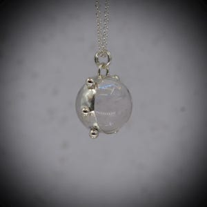 May include: A silver pendant necklace. The pendant has a clear, rounded stone set in a silver metal casing with small, decorative silver accents. The necklace chain is silver. The pendant is spherical in shape.