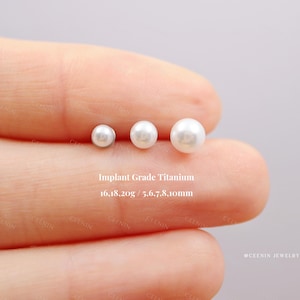 May include: Three white pearl earrings of different sizes are shown on a finger. The text "Implant Grade Titanium" and size measurements are visible. The earrings are 5.6, 7, 8, and 10mm in diameter.