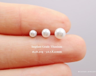 Può includere: Tre orecchini di perle bianche di diverse dimensioni sono mostrati su un dito. Il testo "Implant Grade Titanium" e le misure sono visibili. Gli orecchini hanno un diametro di 5,6, 7, 8 e 10 mm.