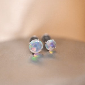 K&ouml;nnte beinhalten: Ein Paar silberne Ohrstecker mit schillernden Opal-Steinen.