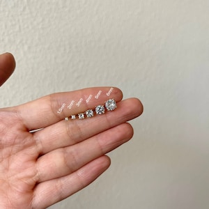 Pu&ograve; includere: Un set di sette orecchini a perno in zircone cubico trasparente di diverse dimensioni, che vanno da 1,5 mm a 6 mm, mostrati su una mano.