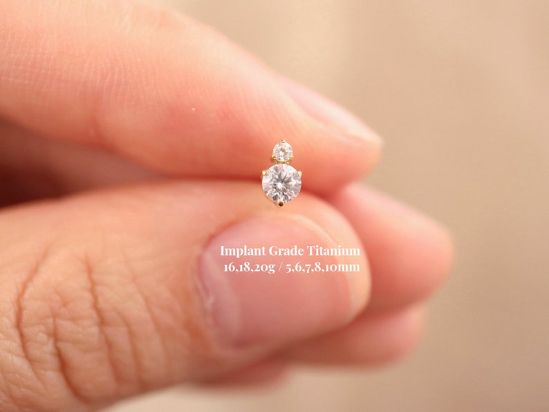 Puede incluir: Un primer plano de un peque&ntilde;o pendiente de diamante transparente con un peque&ntilde;o acento de diamante. El pendiente est&aacute; hecho de titanio de grado implantable y mide 16.18.20g / 5.6.7.8.10mm.