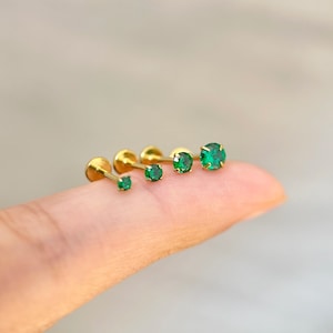 May include: Four gold body jewelry pieces with green gem stones. The pieces are lined up in order of size, with the smallest on the left and the largest on the right.